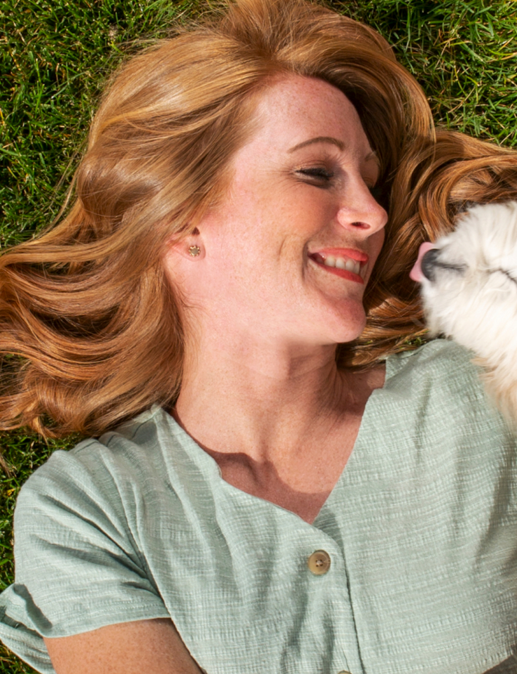 Woman laying on the grass next to her dog.