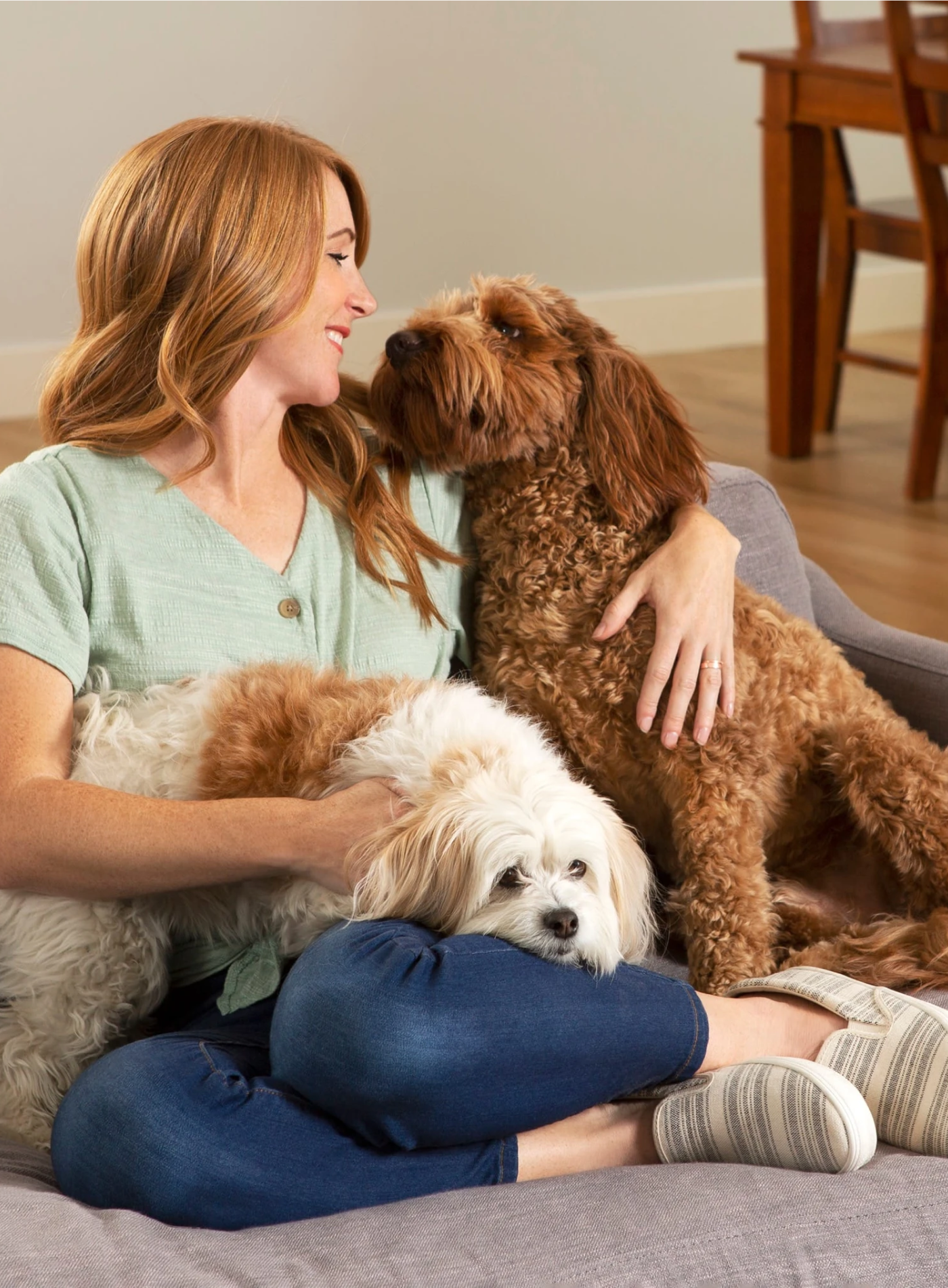 Woman sitting on the couch with two dogs and smiling at one of them.