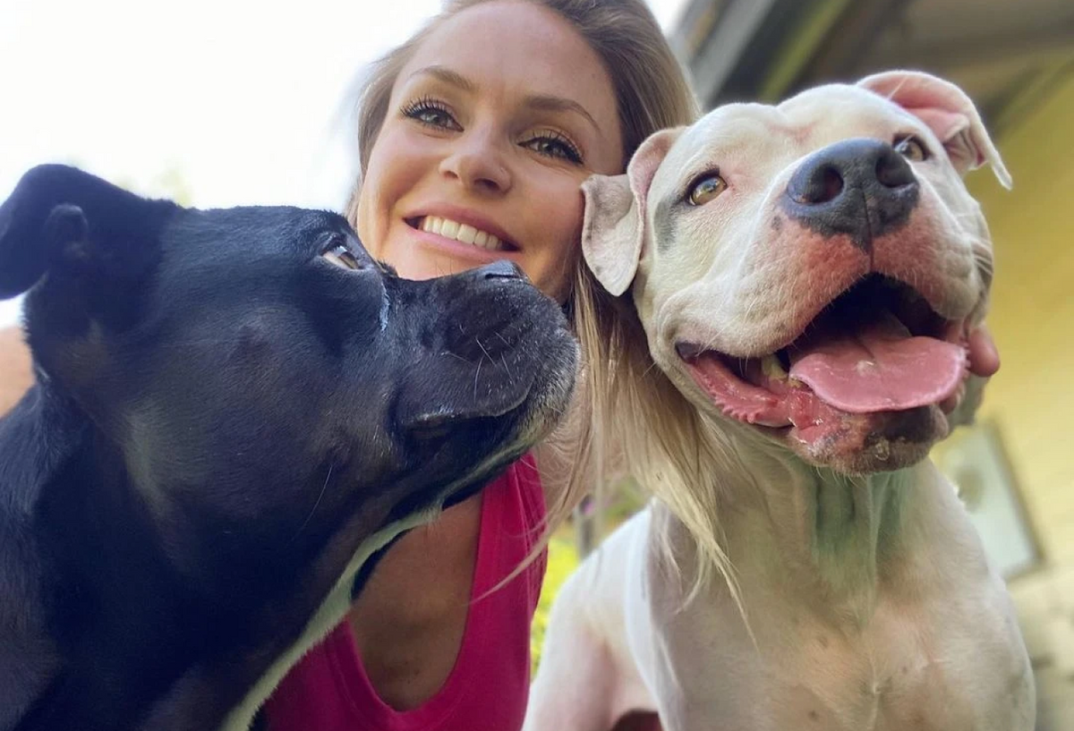 woman smiling with one black and one white dog.